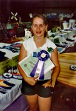 girl smiles, holds notebook and rosette ribbon