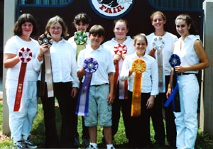 eight livestock showmen wearing white pose with large colorful ribbons